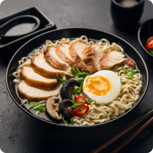 Bol de ramen au poulet grillé, œuf mollet, shiitakés et piment sur fond noir